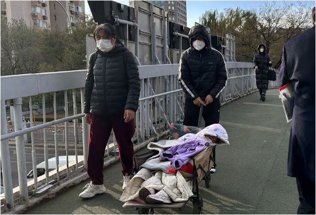 مردی در 27 نوامبر 2023، کودکی را در گاری کمپینگ روی پل هوایی نزدیک بیمارستان کودکان در پکن، چین هل می‌دهد